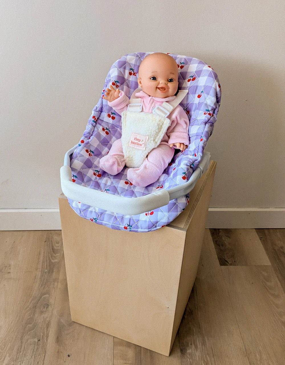Coquille Tiny Harlow Vichy lilas et cerise pour transporter votre poupée partout. Poignée, sangles sécurisées et housse amovible lavable. Jouet d’imitation pour enfants dès 3 ans.